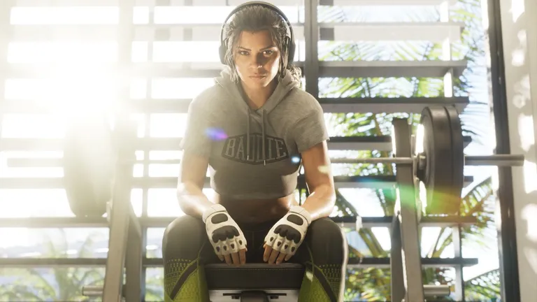 Lucia in a crop hoodie and lifting gloves on a bench press in a sunlit gym