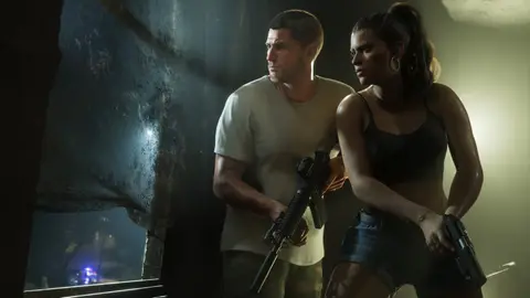 Jason with a carbine and Lucia with a pistol pressed against a wall in a dark room, police lights outside the window
