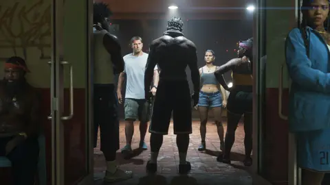 Jason and Lucia walking into a trap house lobby at night while the crowd inside watches them