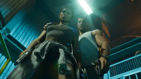 Low-angle shot of Lucia and Jason standing over the camera with pistols drawn under a strip light