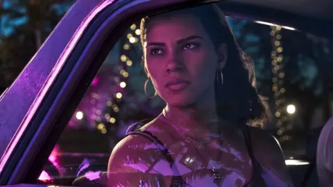 Lucia in the passenger seat at night, neon and string lights reflected in the windscreen