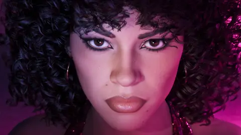 Close-up of Lucia with a curly seventies hairstyle and sequin dress under pink club light